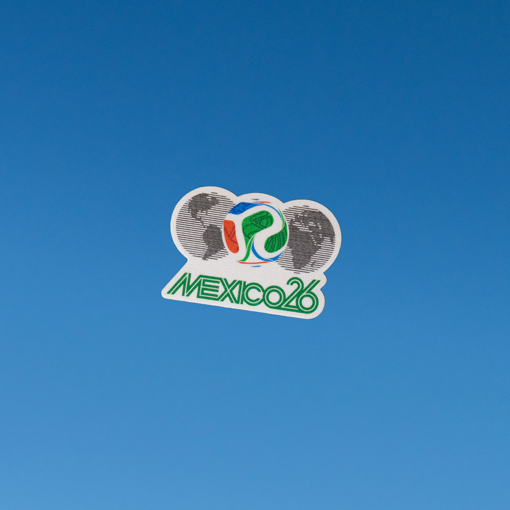 Sticker Mexico 26 – Volver a Primera Sticker Mexico 26 con balón multicolor al centro y siluetas del mapa mundial en fondo sobre azul
